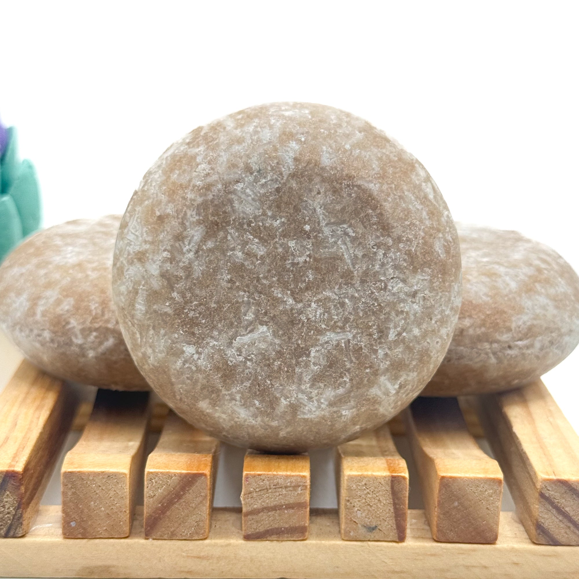 Three tan zero waste rice protein shampoo bars on a wooden surface with a white background