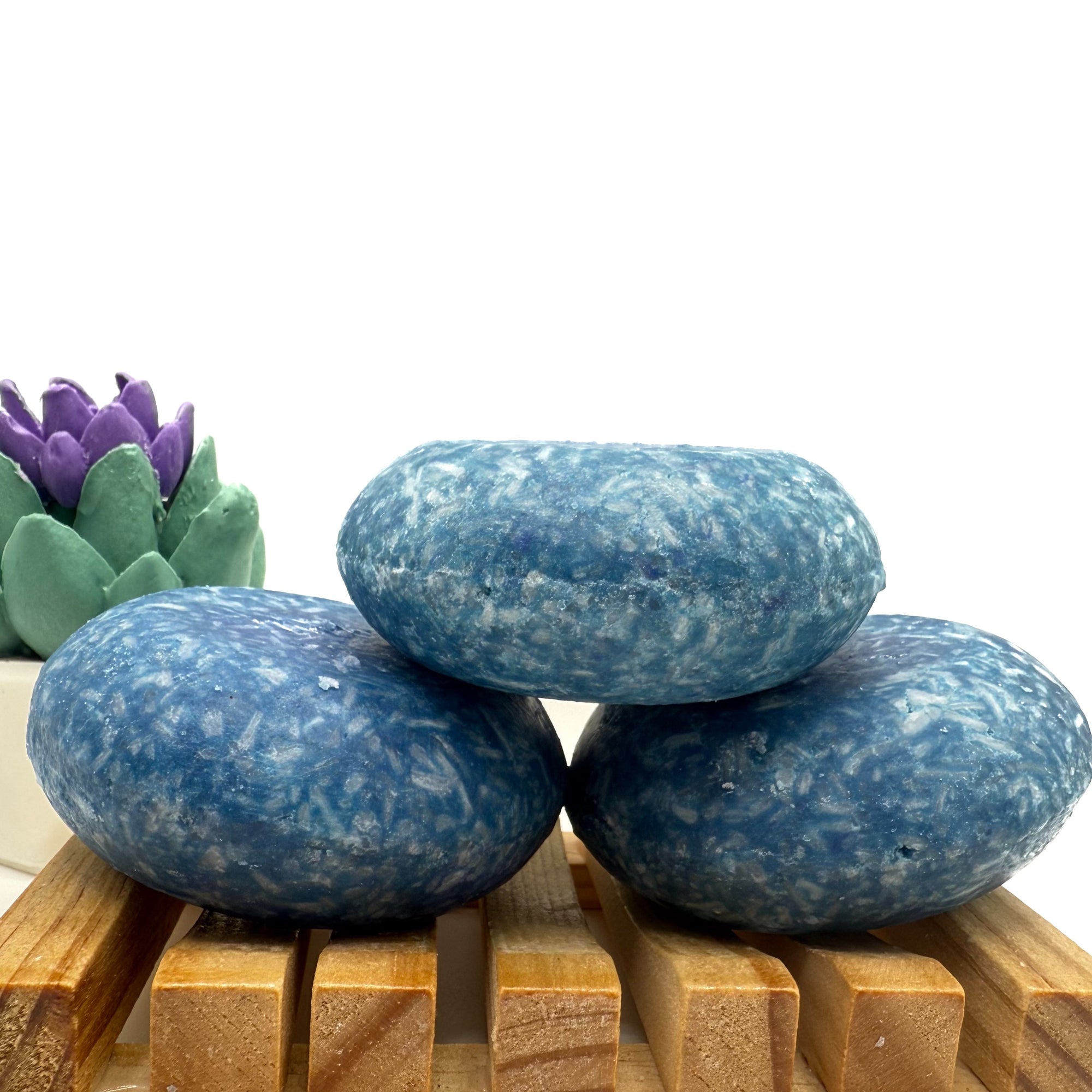 Three Blueberry shampoo bars sitting on. wood soap dish stacked on top of each other.