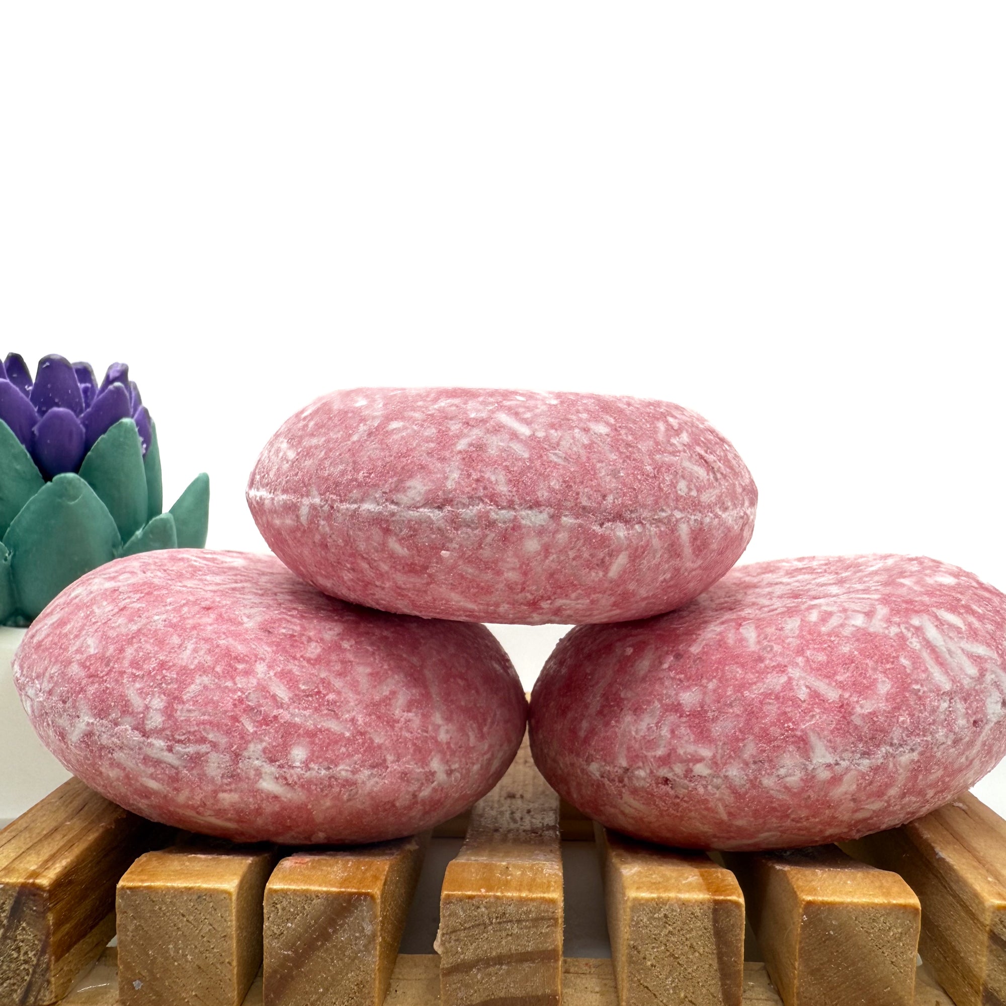 Three Raspberry Lime shampoo bars sitting on. wood soap dish stacked on top of each other.