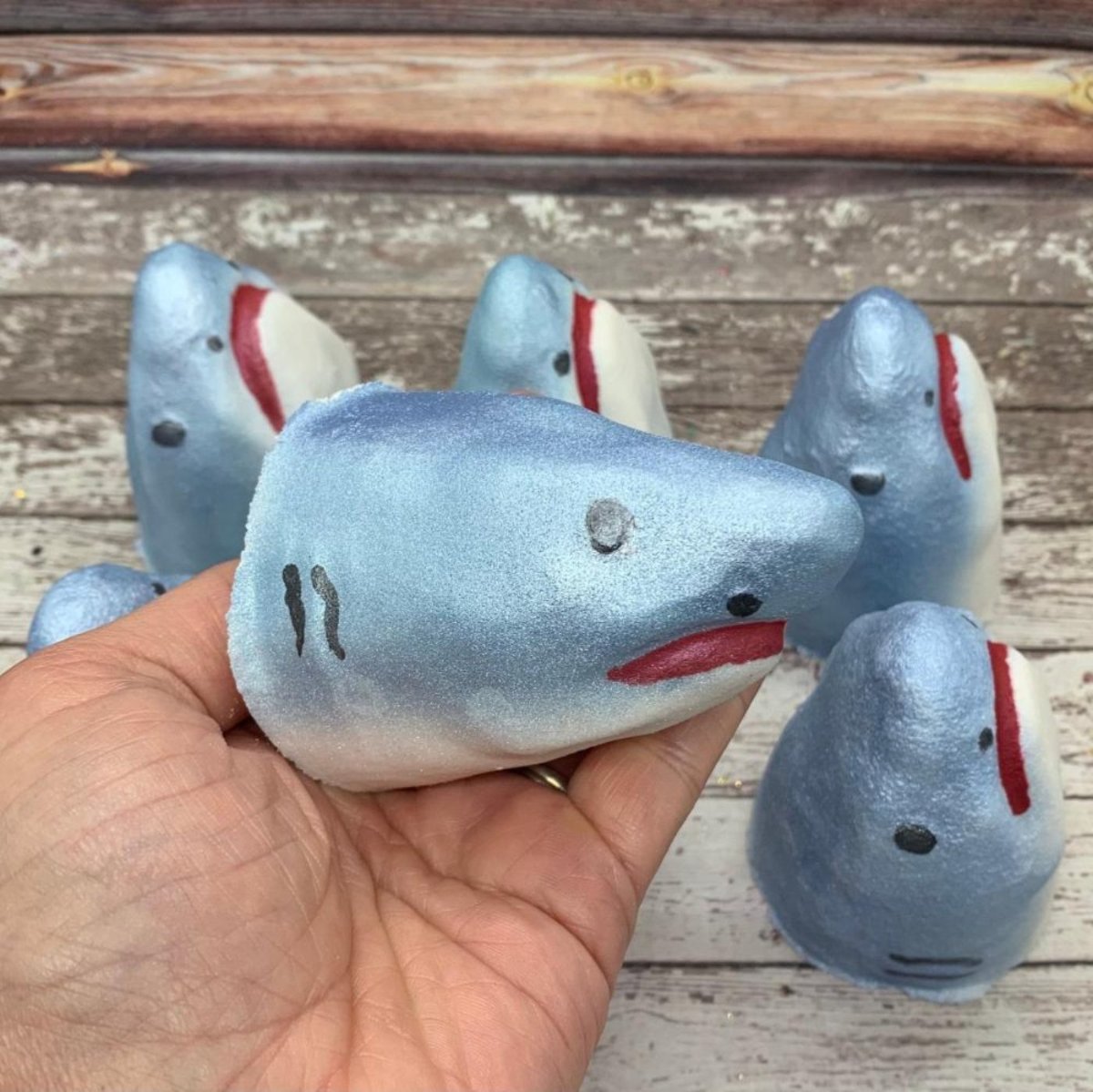 One shark head shaped bath bomb airbrushed silvery-blue hand-painted black eyes and gills and a red mouth. Five others swimming around!