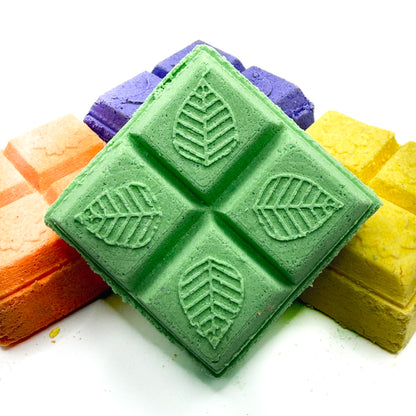 Green eucalyptus square shower steamer with other with orange and yellow shower steamers in the background on a white background 