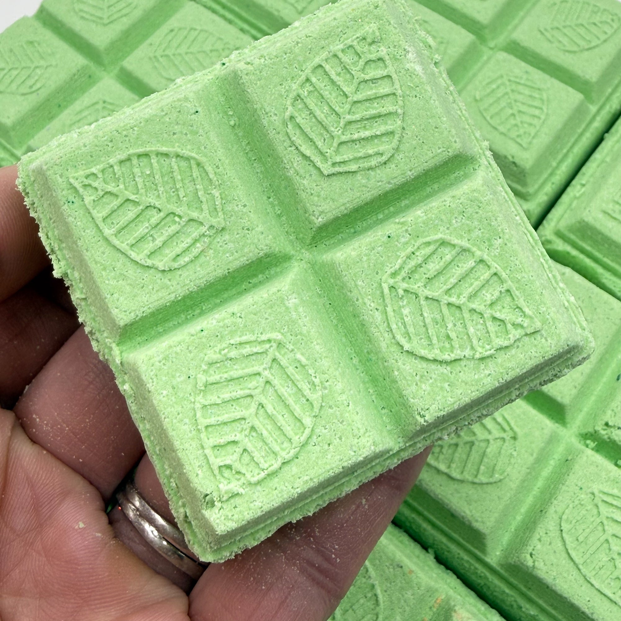 Green eucalyptus shower steamer with leaf pattern held by a hand. 