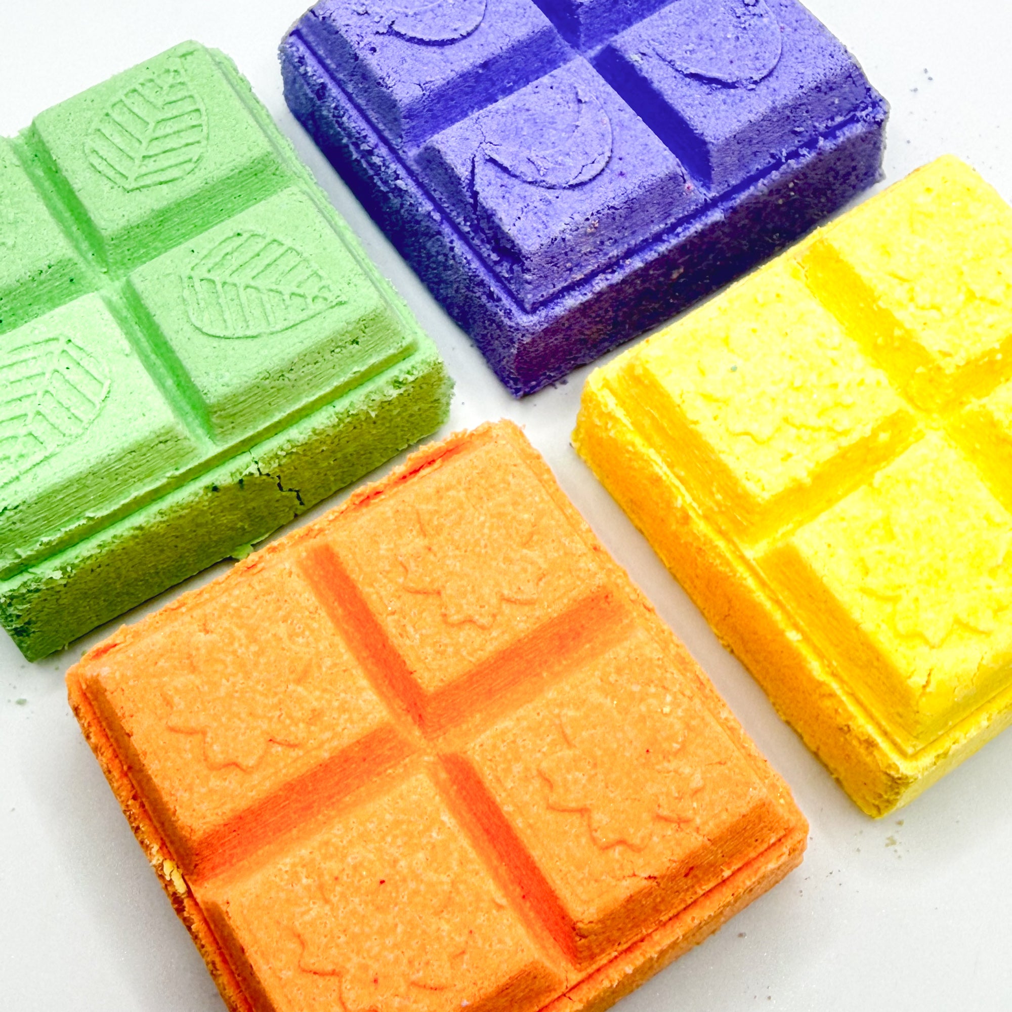 Four orange, yellow, green, purple square shower steamer on a white background 
