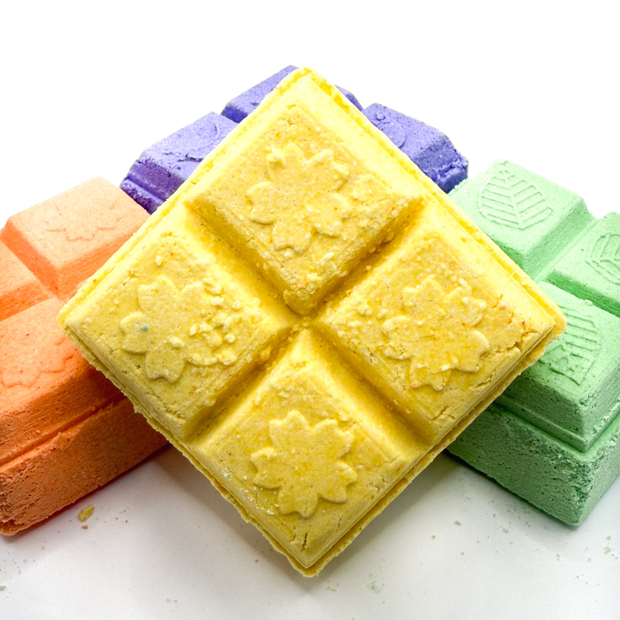 Yellow lemon square shower steamer with other with orange and green shower steamers in the background on a white background 