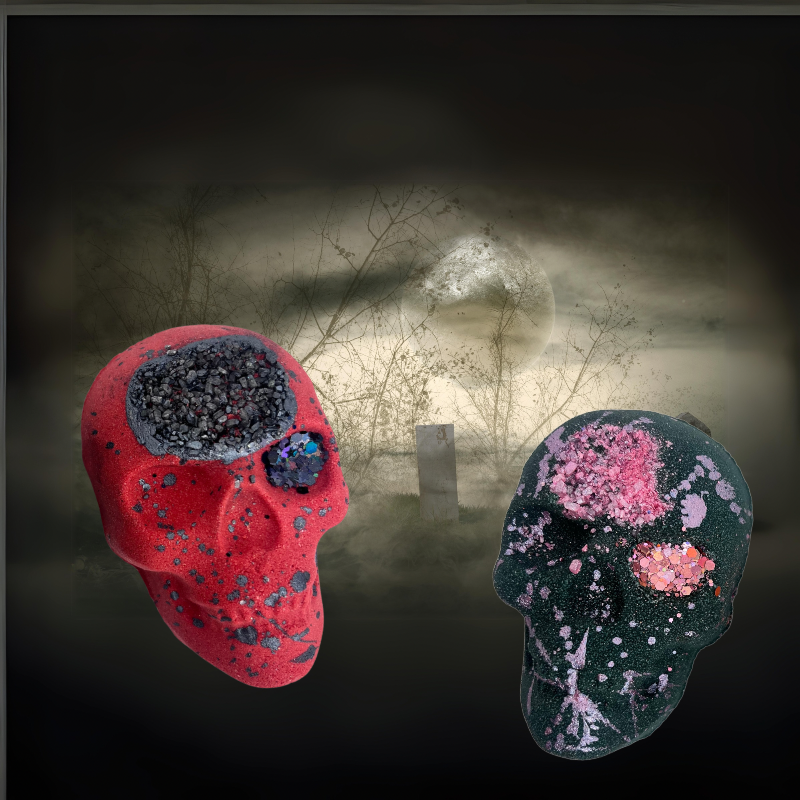 One red and one black skull shaped bath bomb from Rusted Acre Soap Company displayed on an eerie background with a cloudy full moon.