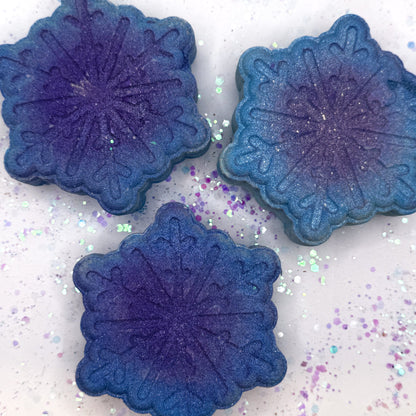 Three blue snowflake shaped  bath bombs made by Rusted Acre Soap Co on a glittery surface