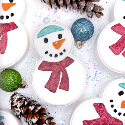 Handmade snowman bath bomb with colorful scarf and accessories on a glittery background. Made by Rusted Acre Soap Co.