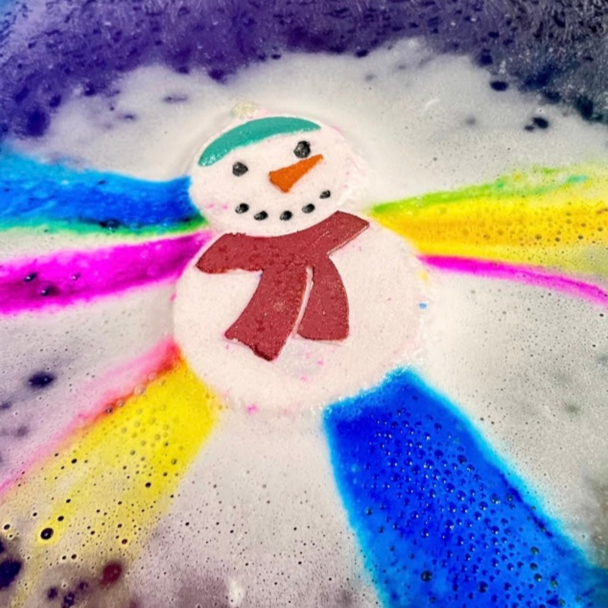Colorful snowman bath bomb with rainbow swirls in a bathtub tub. Hand made by Rusted Acre Soap Co.