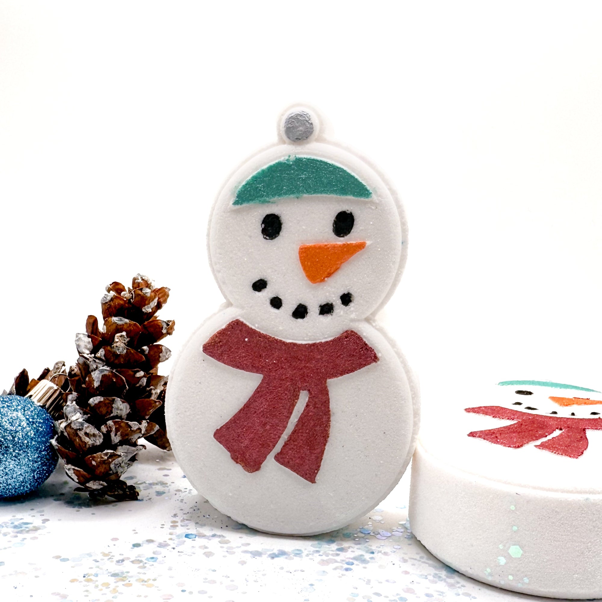 Decorative snowman bath bomb with a pine cone and blue ornament on a white background. Made by Rusted Acre Soap Co.