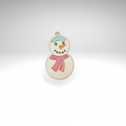 One white snowman shaped bath bomb from Rusted Acre Soap Co. Hand-painted with a blue hat, snowman face and a red scarf. 