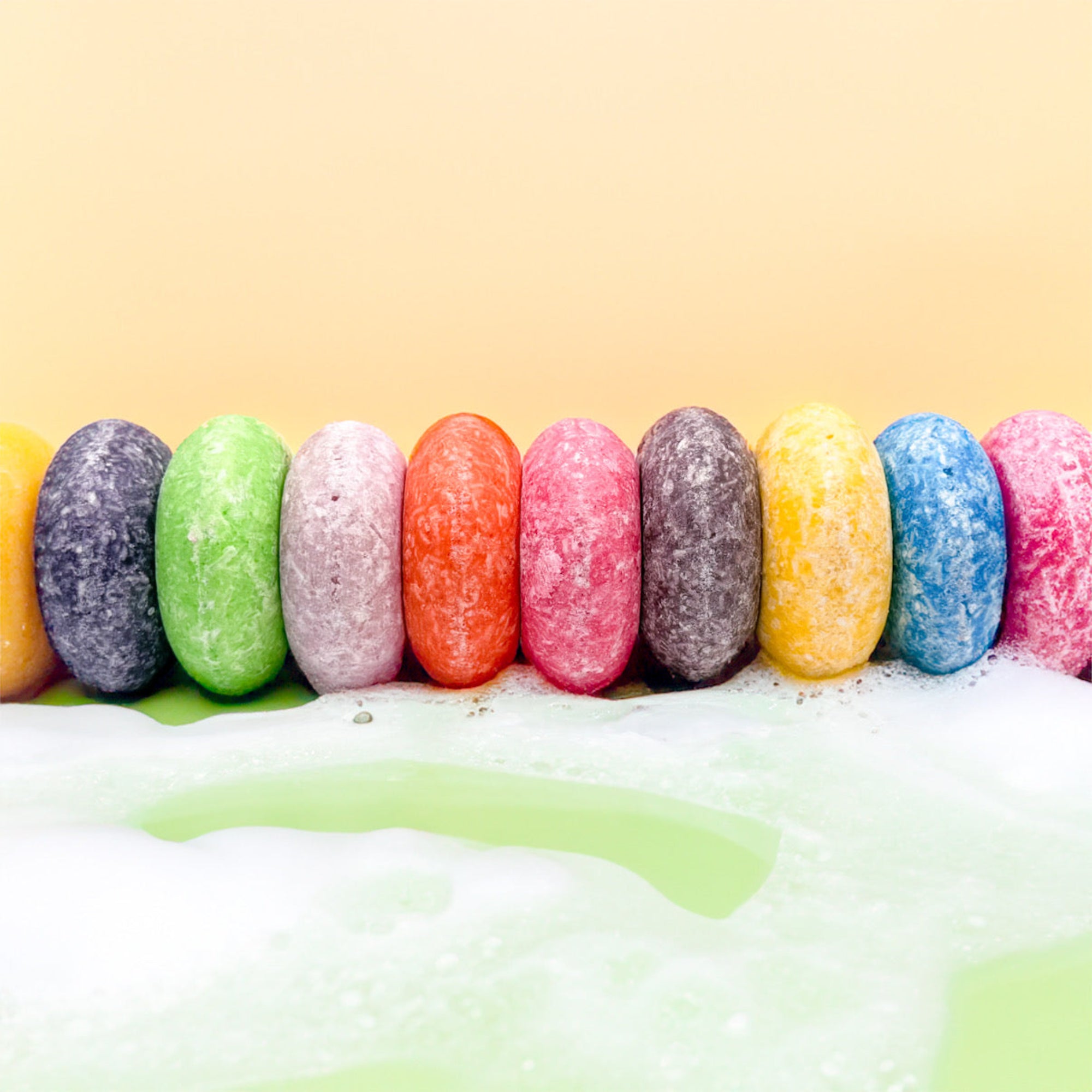 A row of solid shampoo bars sitting in shampoo foam on a fun colorful background.