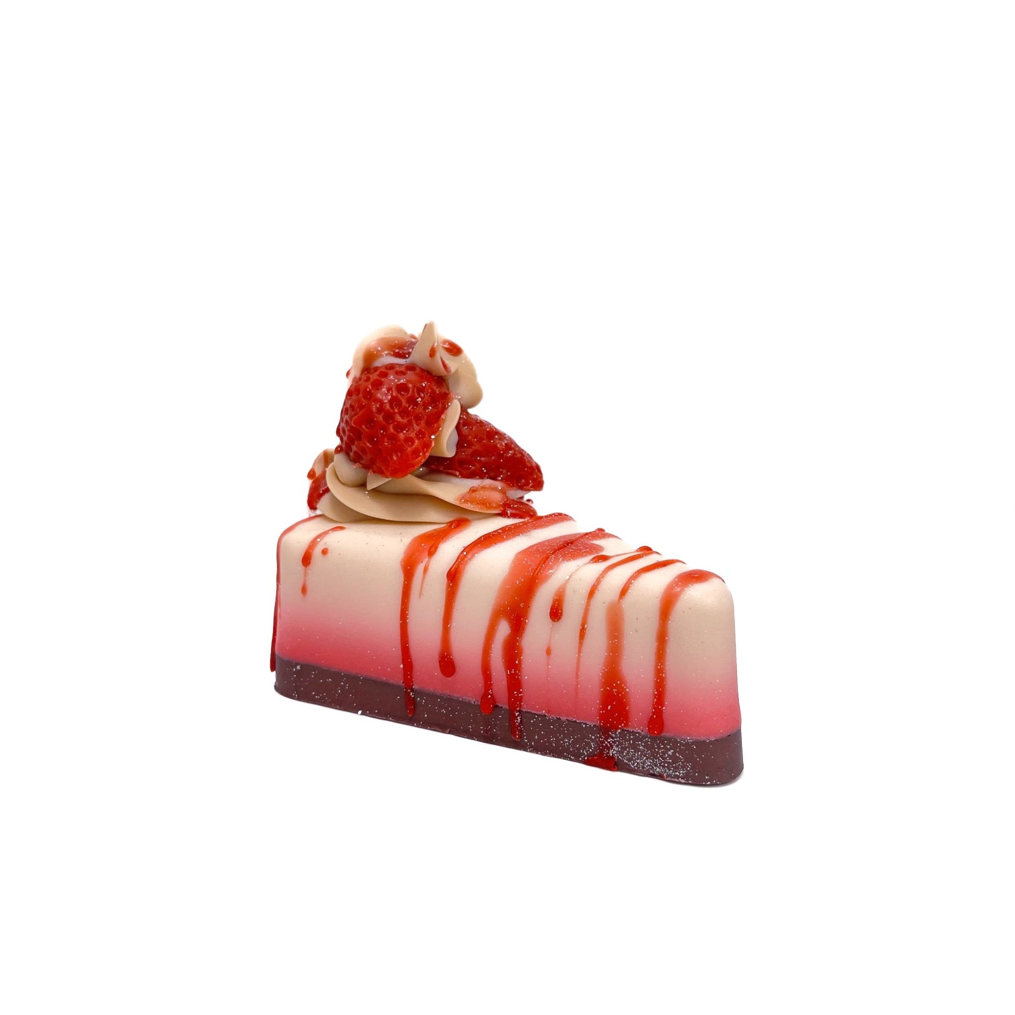 A slice of strawberry cheesecake pie shape soap from Rusted Acre Soap Co. Filling is white fading to red. The crust is dark. Topped with a cold process soap puff and red strawberry soap embeds.