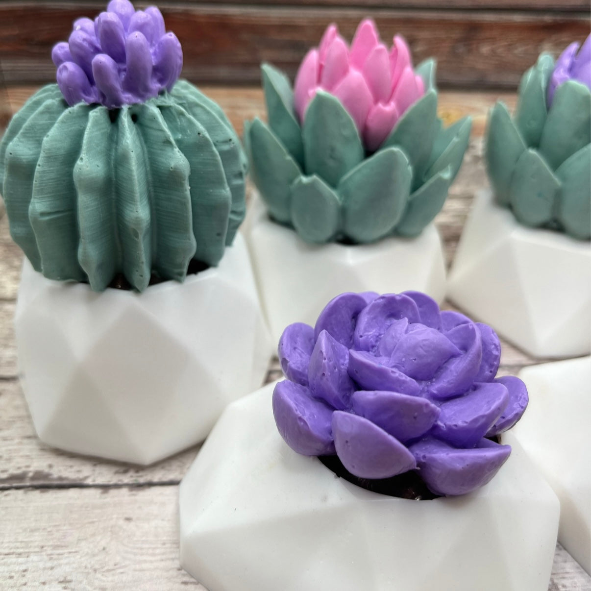 3 decorative succulent soaps with 2 purple and one pink flower and a white flower pot. 