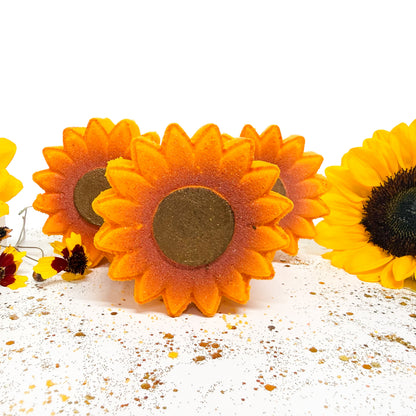 Three handmade sunflower bath bombswith orange and yellow petals and dark brown centers, arranged on a white surface with scattered flower petals.