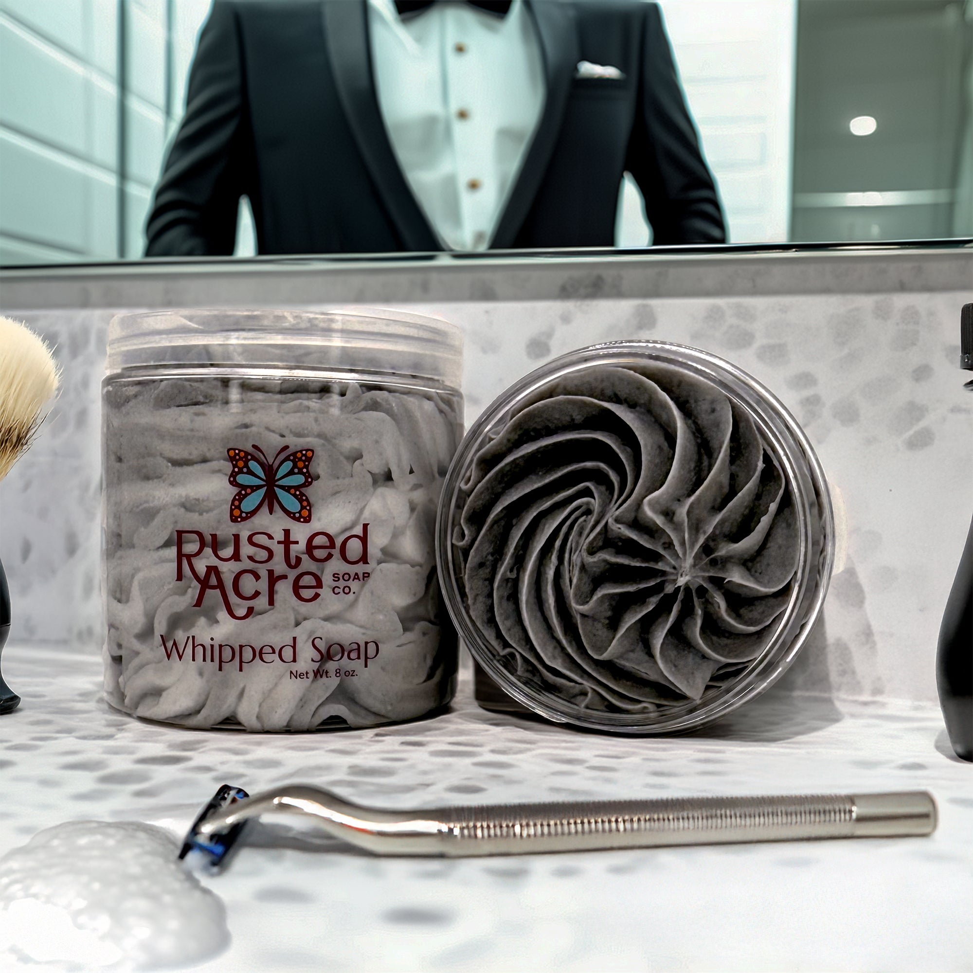Two Jars of tuxedo whipped soap made by Rusted Acre Soap Company in a bathroom with razor.