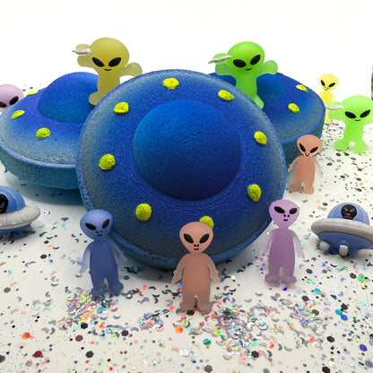 One blue and yellow UFO bath bomb showing the front profile with two bath bombs on a white background with alien toys placed around the bath bombs.