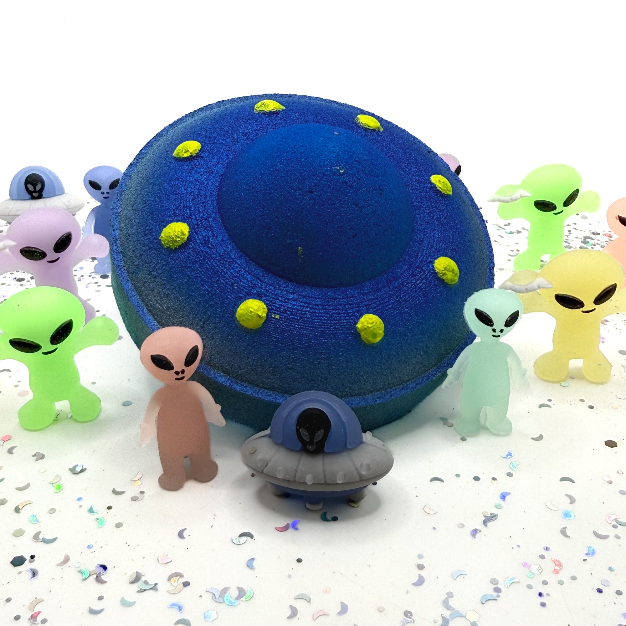 Blue and yellow Ufo bath bomb with little alien toys scattered around 