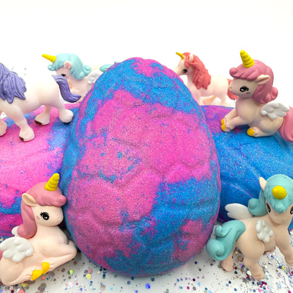 Blue and pink unicorn egg bath bomb with unicorn figurines on a white background. 