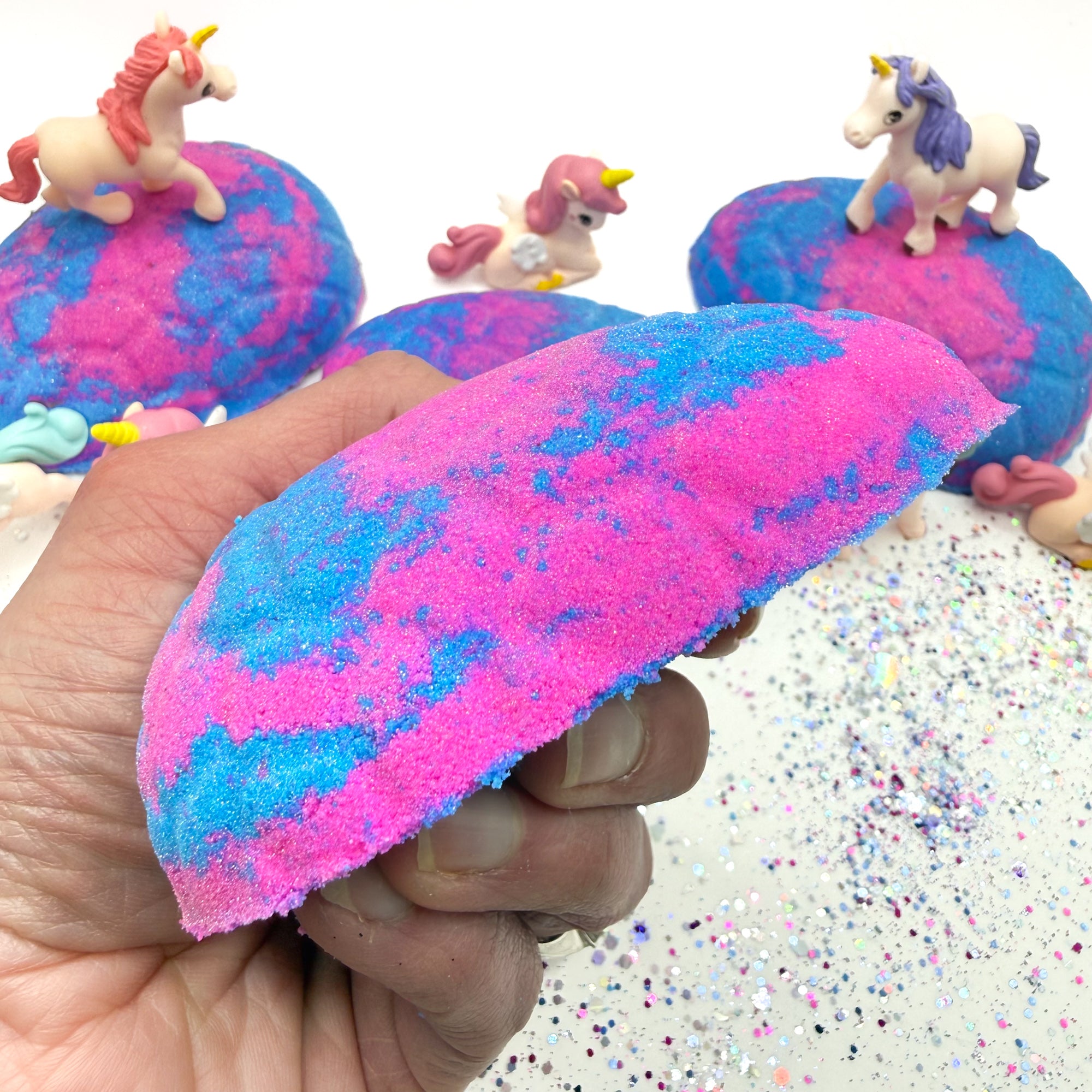 Side view of Rusted Acre Soap Co's Unicorn Egg bath bomb with unicorn figures on a glittery surface.