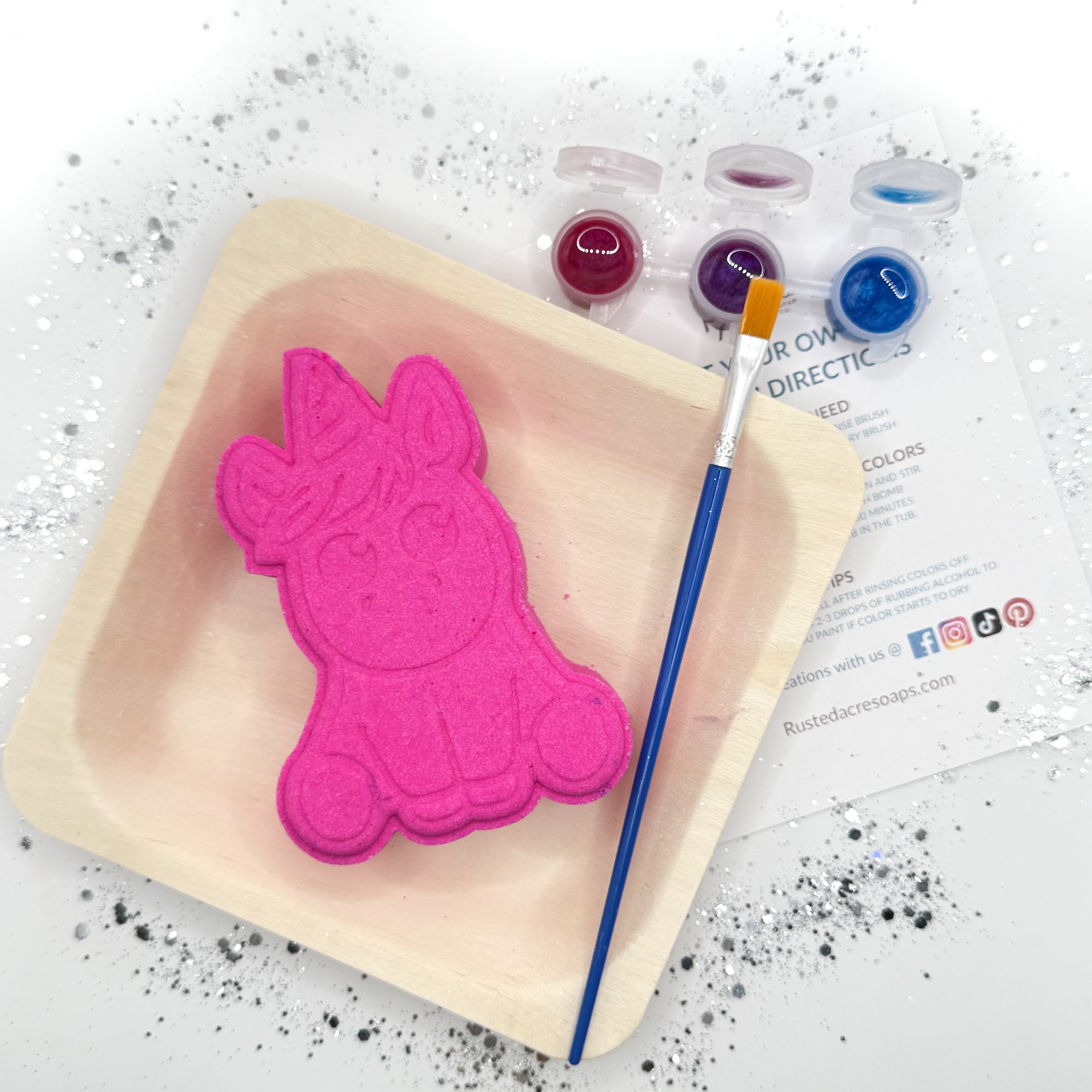 Full kit view of one pink paint your own unicorn shaped bath bomb displayed with a paint brush, paint pots with color.