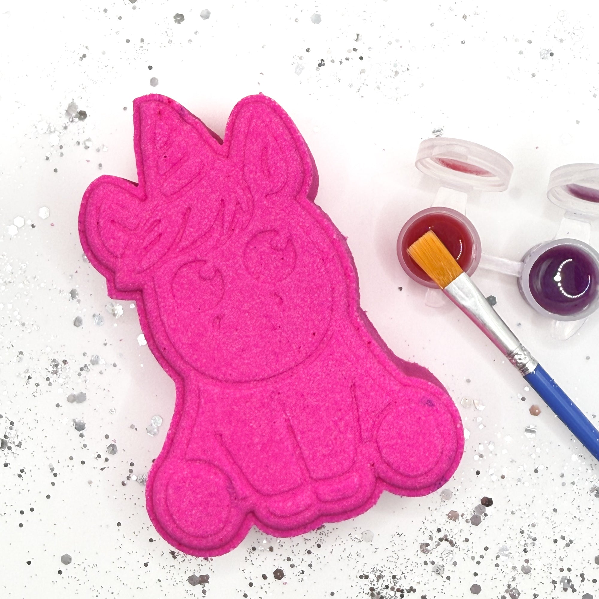 Top view of one pink paint your own unicorn shaped bath bomb with a paint brush, paint pots with color.