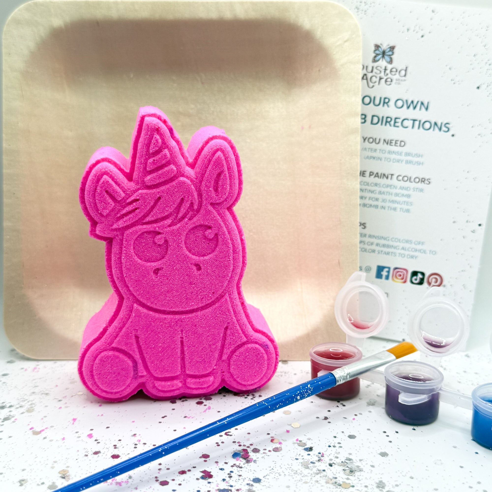 One pink paint your own unicorn shaped bath bomb displayed with a paint brush, paint pots with color.