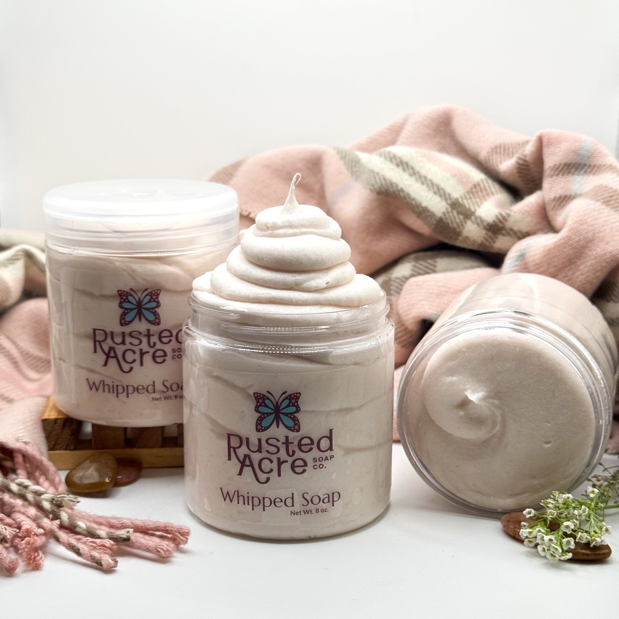 Three jars of Rusted Acre Soap CO’s cashmere whipped soap with different views on a white background with photo props. 