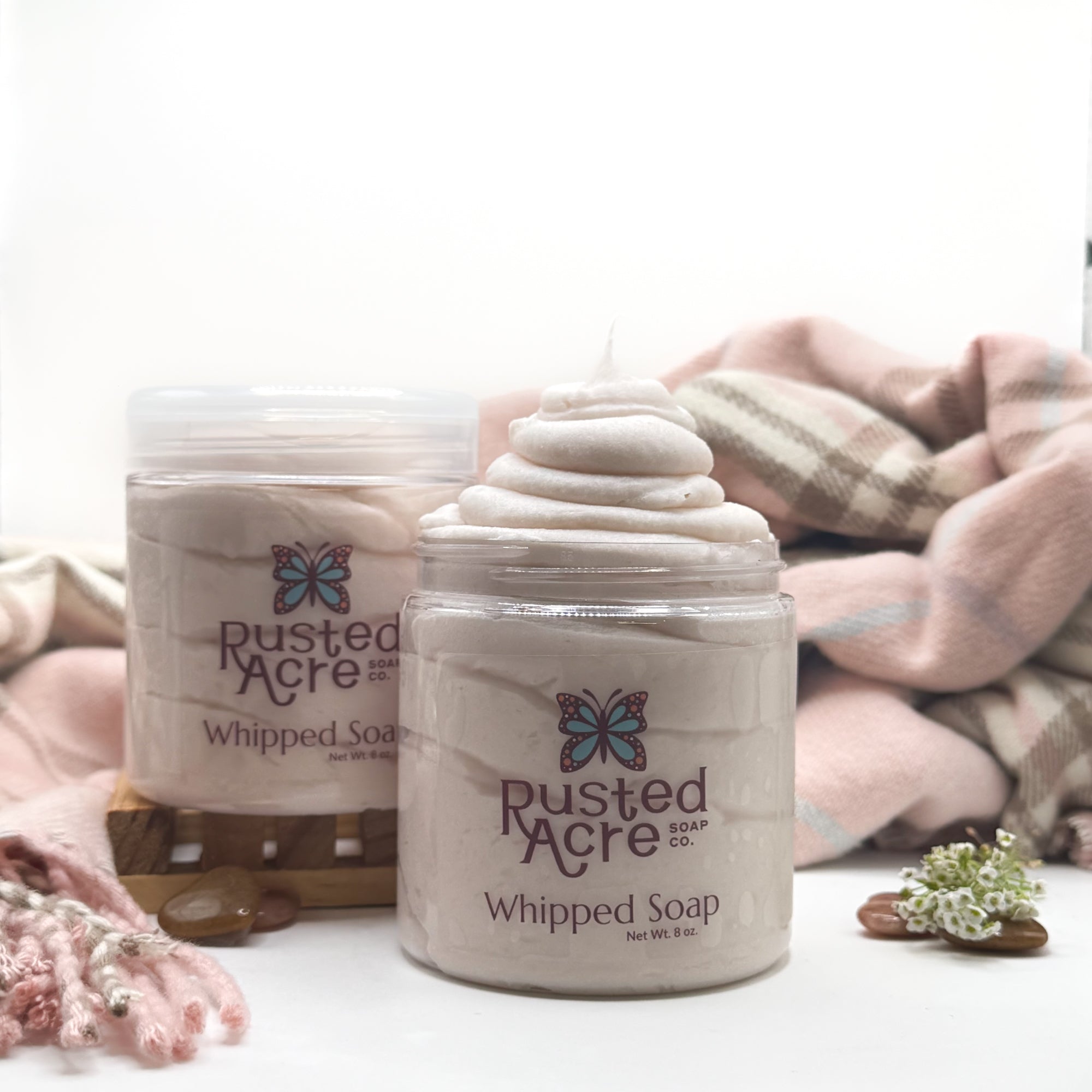 Two jars of Rusted Acre Soap CO’s cashmere whipped soap on a white background with photo props. 