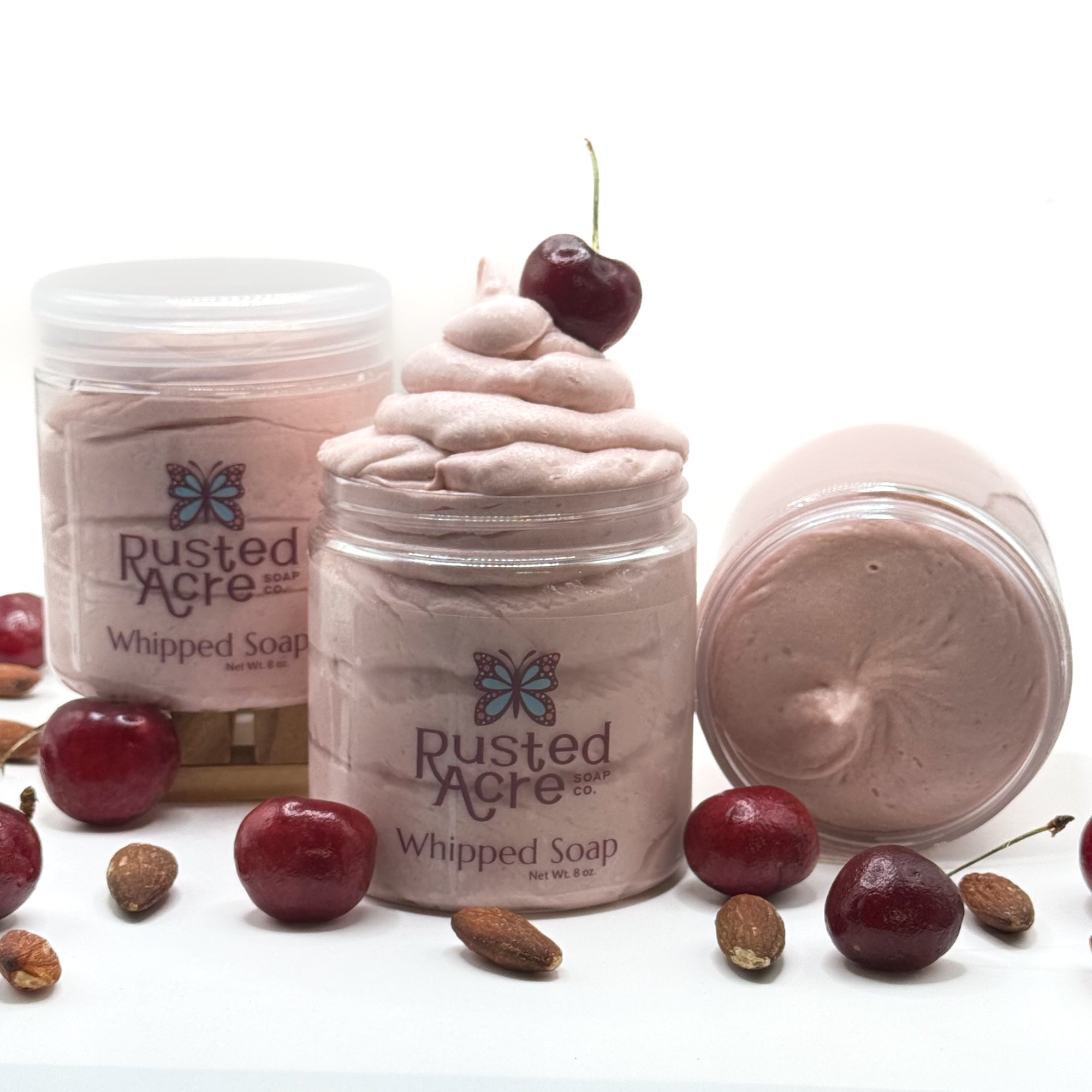 Three jars of light red cherry almond whipped soap with cherries and nuts on a white background.