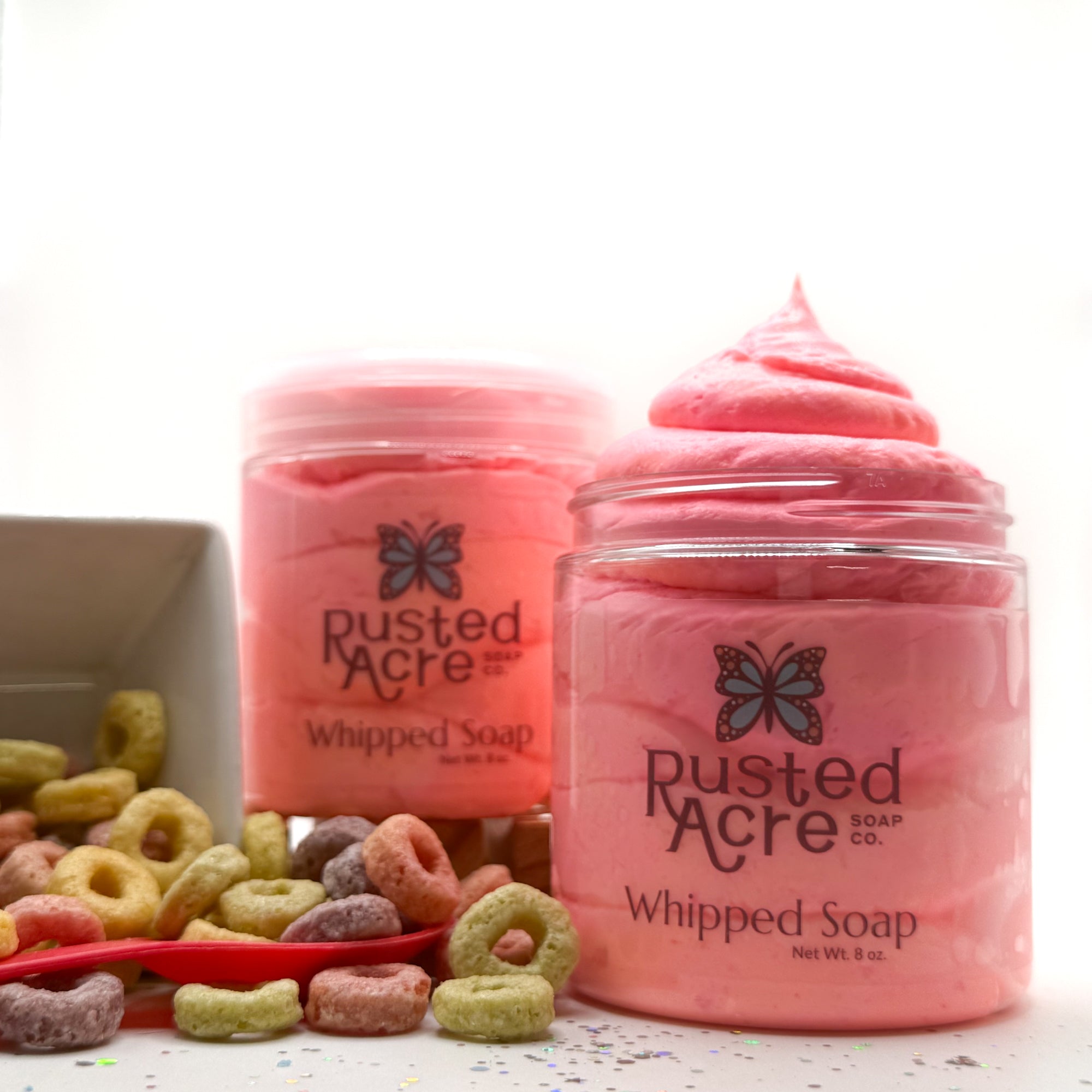 Two jars of Rusted Acre whipped soap with colorful fruity cereal circles in the background.