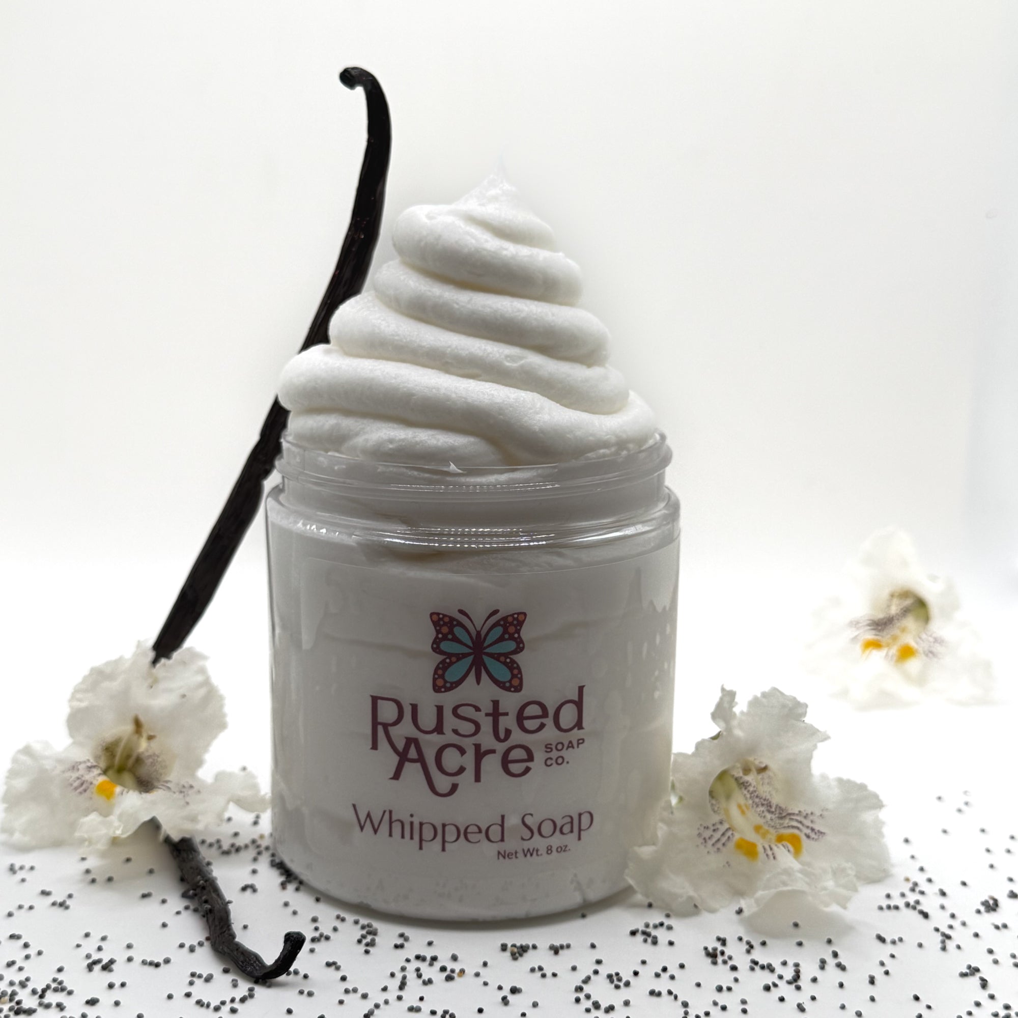 Jar of Rusted Acre vanilla whipped soap with a vanilla bean and flowers on a white background