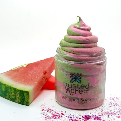 Pink and green swirled watermelon twist whipped soap in a jar with a slice of watermelon on a white background