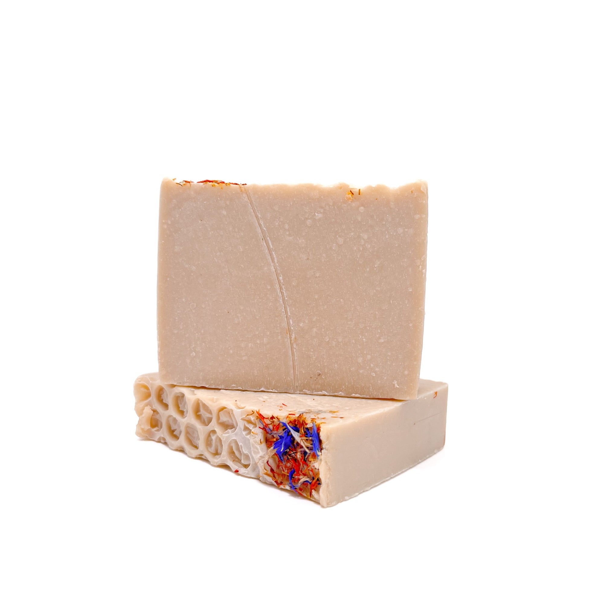 Two bars of natural colored wildflower and honey soap from Rusted Acre Soap Co. One upright and one lying flat to show texture. Red and blue flower petals on top. 