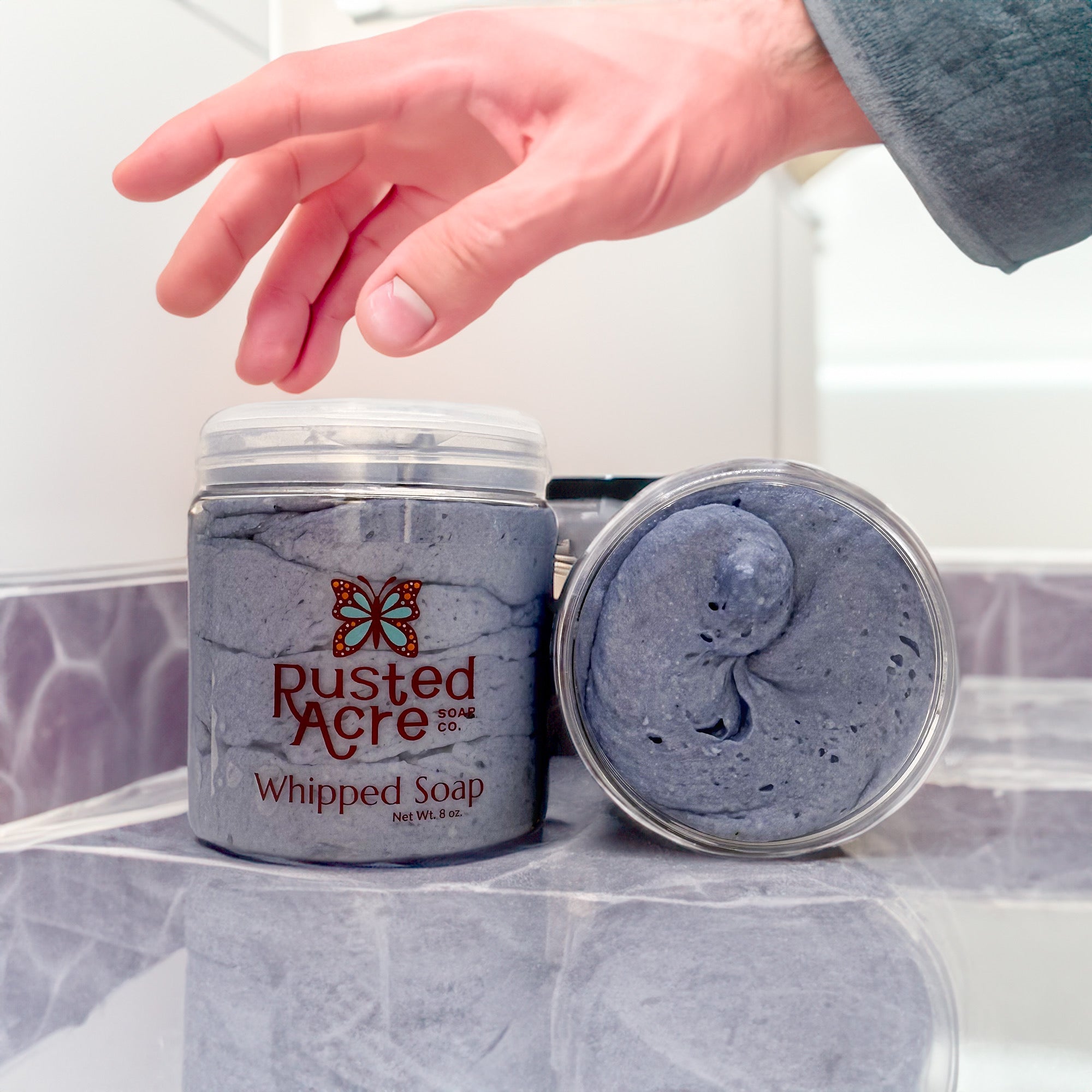Two jars of Rusted Acre Soap Company’s zephyr whipped soap front and top view in a lifestyle setting.